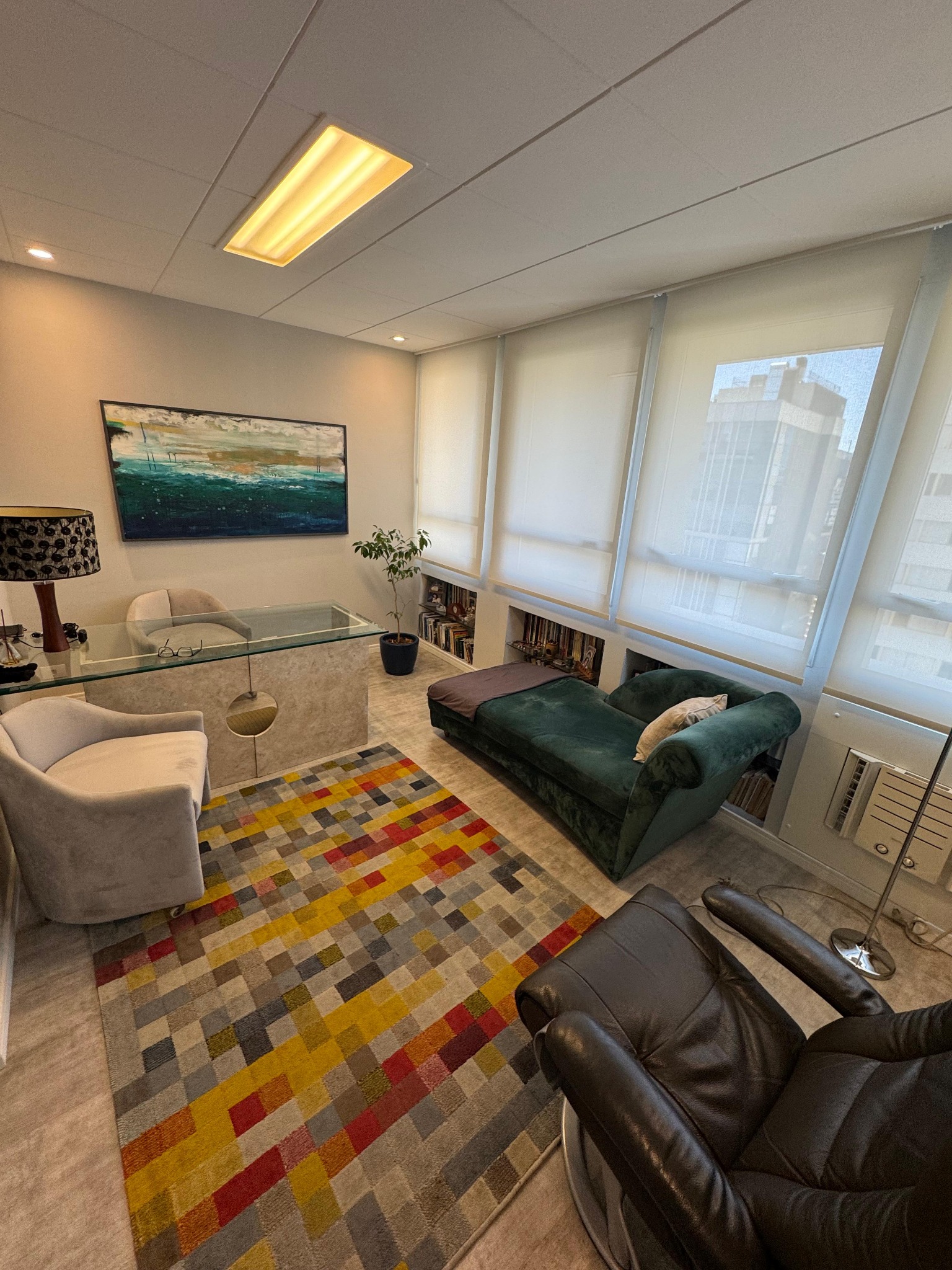Sala de atendimento aconchegante, com poltronas, divã, escrivaninha e muita luz natural
